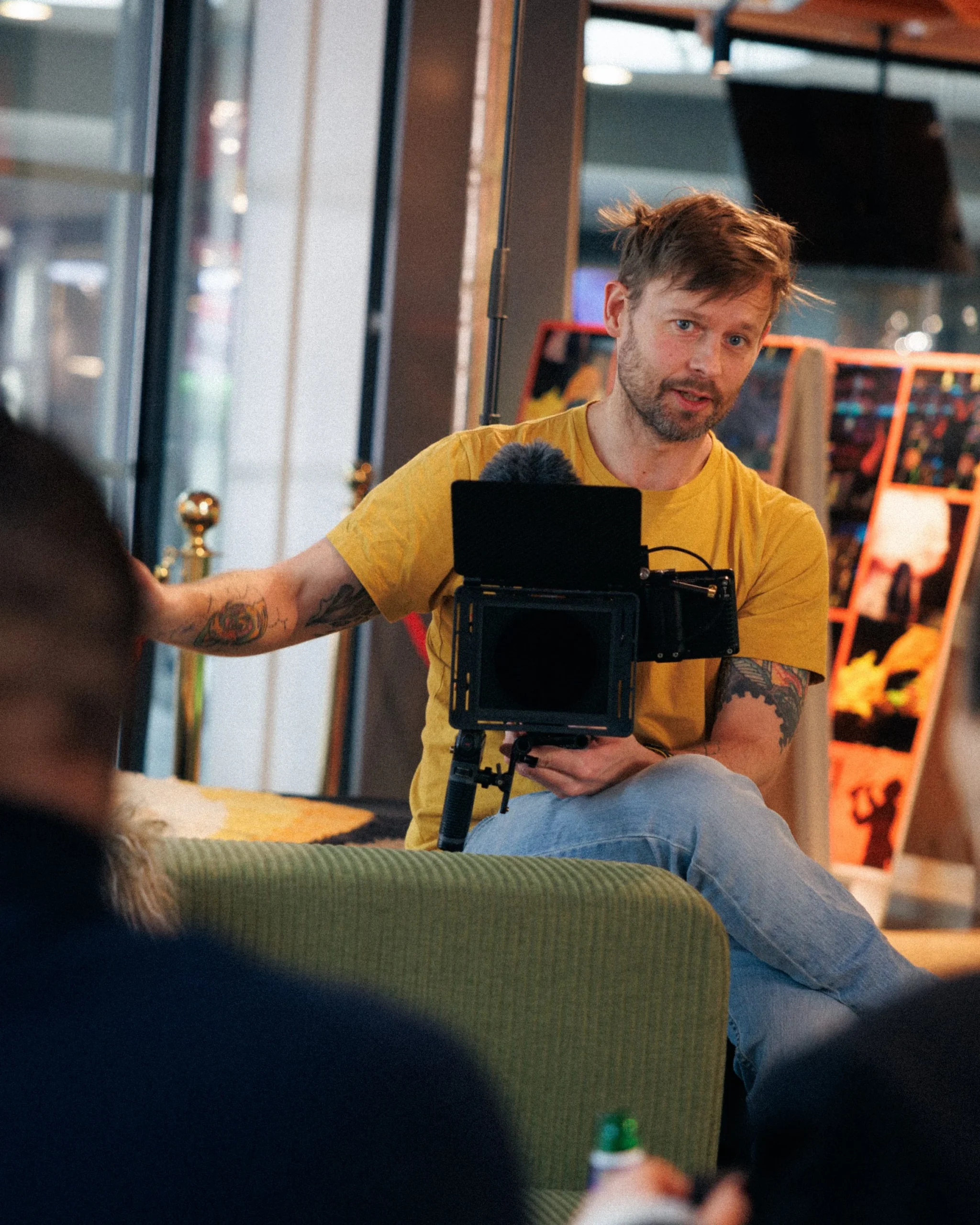 Robin Danehav in a yellow T-shirt, seated with a cinema camera during an interview.