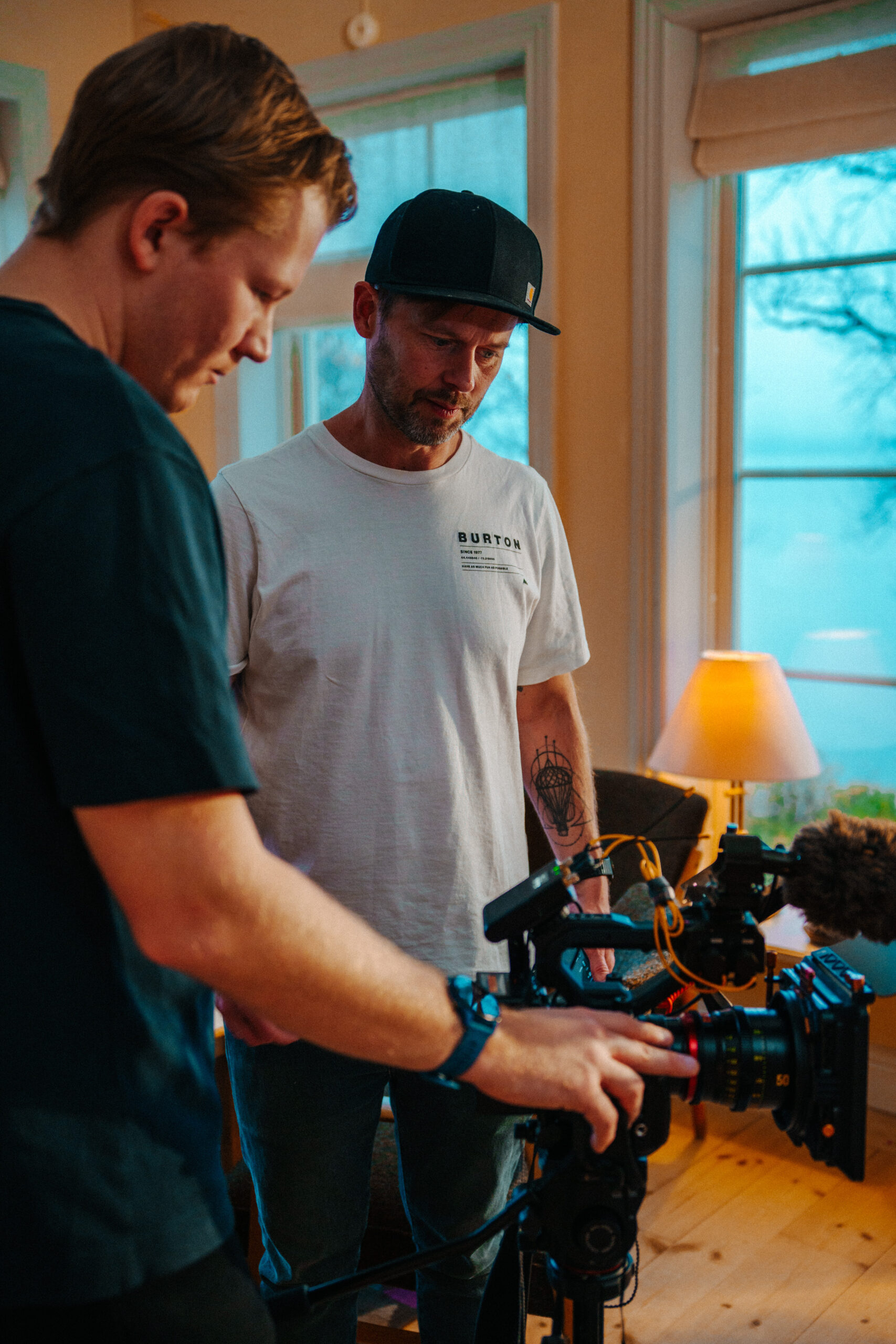 Isak Friberg adjusting a cinema camera while Robin Danehav looks on, in a room with a window to the mountains.